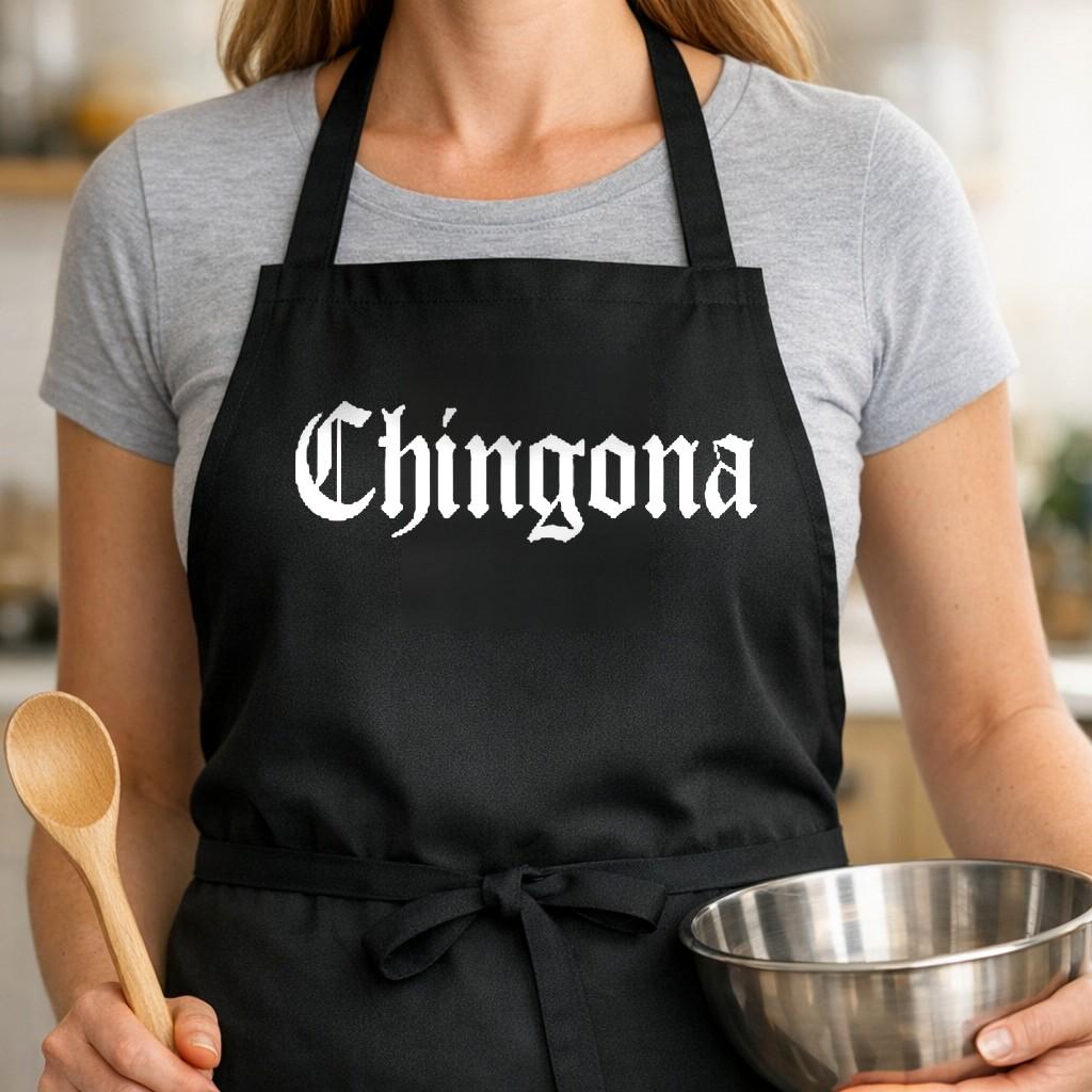 Chingona black BBQ apron, woman torso close-up: Black apron with white gothic style text reading 'Chingona' centered on front in bold lettering