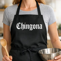 Chingona black BBQ apron, woman torso close-up: Black apron with white gothic style text reading 'Chingona' centered on front in bold lettering