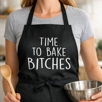 Time to Bake Bitches black BBQ apron, woman torso close-up: Black apron with large white bold text reading Time To Bake Bitches in a casual handwritten style font