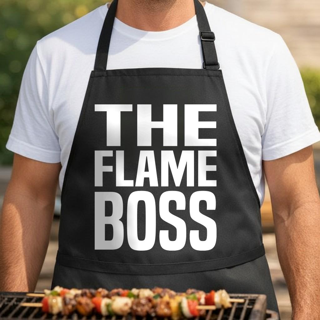 Flame Boss black BBQ apron, torso close-up: Black apron with large white block letters spelling THE FLAME BOSS in bold uppercase font.