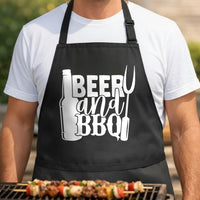 Beer and BBQ black BBQ apron, torso close-up: Black apron with white graphic of a beer bottle, barbecue fork, and the words Beer and BBQ in bold, stylized font.