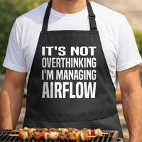 Managing Airflow black BBQ apron, torso close-up: Black apron with large bold white text reading It’s Not Overthinking I’m Managing Airflow in block letters