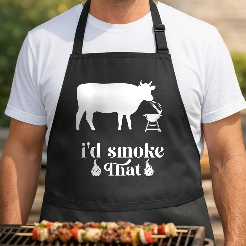 I'd Smoke That black BBQ apron, torso close-up: Black apron with white silhouette of a cow, a charcoal grill, and the phrase I'd Smoke That with flame illustrations below.