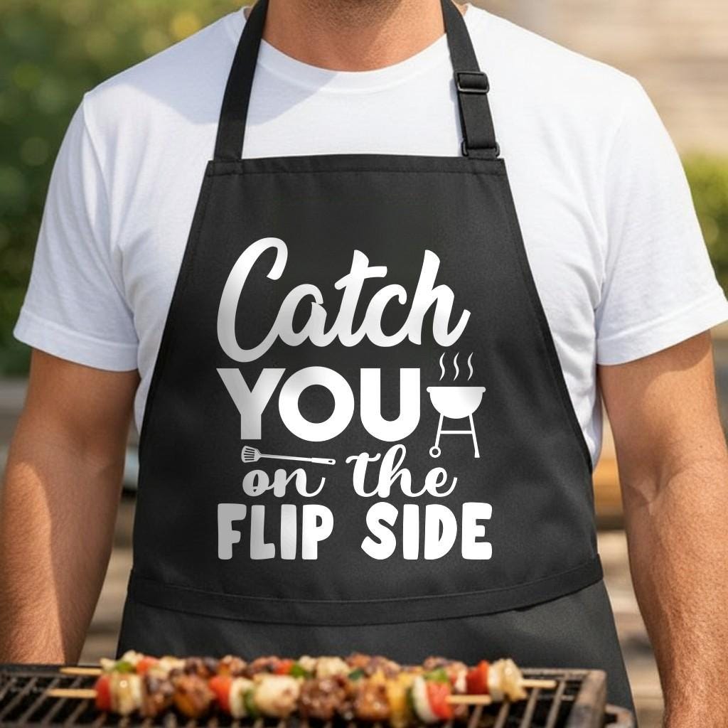 Catch You on the Flip Side black BBQ apron, torso close-up: Black apron with white text saying 'Catch You on the Flip Side' alongside a spatula and a steaming kettle grill graphic