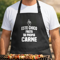 Este Chico Frota Su Propia Carne black BBQ apron, torso close-up: Black apron with bold white text saying Este Chico Frota Su Propia Carne and a white hand graphic pointing upward in a casual style.