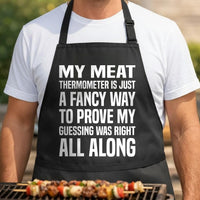 Thermometer Proof Method black BBQ apron, torso close-up: Black apron with bold white text saying my meat thermometer is just a fancy way to prove my guessing was right all along